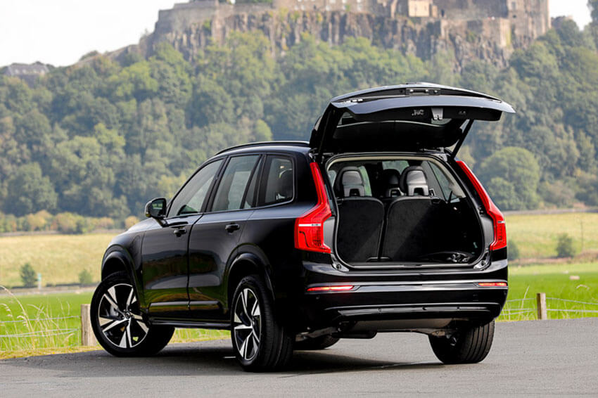 A black Volvo with the boot open showing the rearmost seats with a castle on a hill and grass in the background