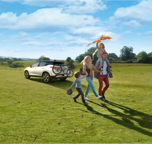 Family running down a grassy hill with car in background